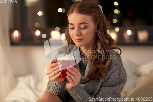 Image of happy woman holding mug with whipped cream in bed