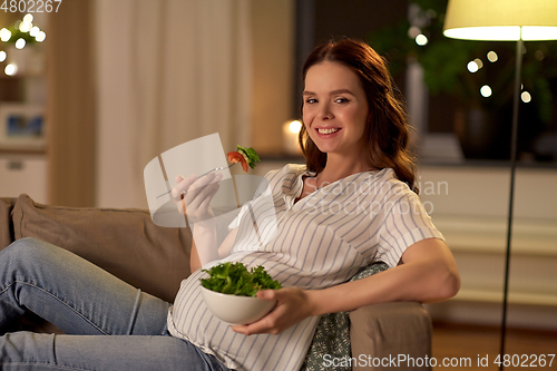 Image of happy smiling pregnant woman eating salad at home