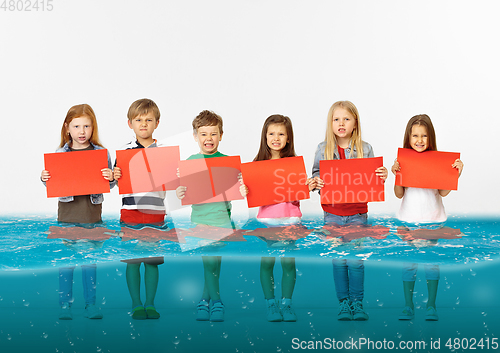 Image of Group of children with blank red banners standing in water of melting glacier, global warming