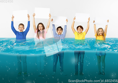 Image of Group of children with blank white banners standing in water of melting glacier, global warming