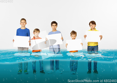 Image of Group of children with blank white banners standing in water of melting glacier, global warming