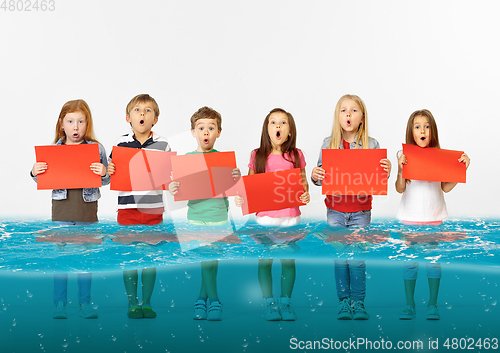 Image of Group of children with blank red banners standing in water of melting glacier, global warming