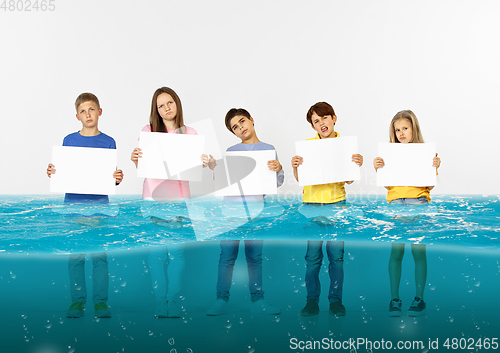 Image of Group of children with blank white banners standing in water of melting glacier, global warming