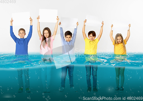 Image of Group of children with blank white banners standing in water of melting glacier, global warming