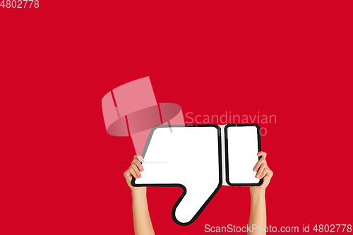 Image of Hands holding the sign of dislike on red studio background