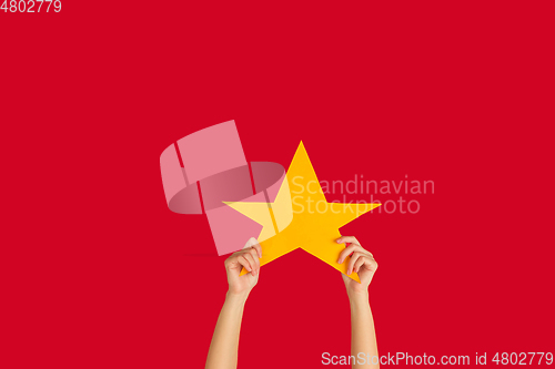 Image of Hands holding the sign of star on red studio background