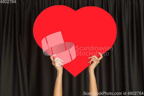 Image of Hands holding the sign of heart on black studio background