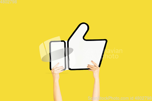 Image of Hands holding the sign of like on yellow studio background