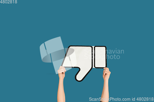 Image of Hands holding the sign of dislike on blue studio background