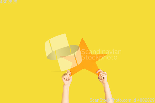 Image of Hands holding the sign of star on yellow studio background