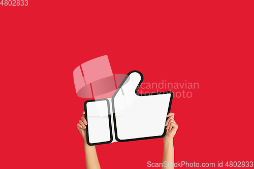 Image of Hands holding the sign of like on red studio background