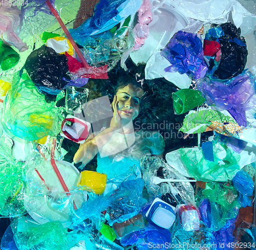 Image of Woman drowning in ocean water under plastic recipients pile, environment concept