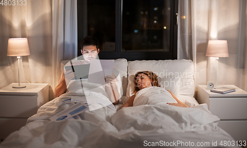 Image of man with tablet computer working in bed at night