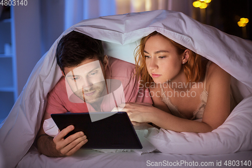 Image of couple using tablet pc in bed at night