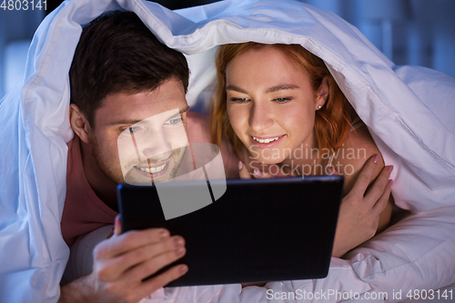 Image of happy couple using tablet pc in bed at night