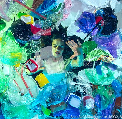 Image of Woman drowning in ocean water under plastic recipients pile, environment concept