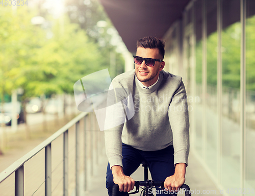 Image of young man in shades riding bicycle on city street