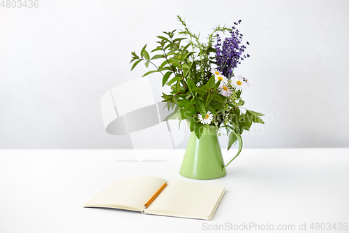 Image of notebook with pencil and bunch of flowers in jug