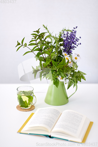 Image of herbal tea, book and flowers in jug on table