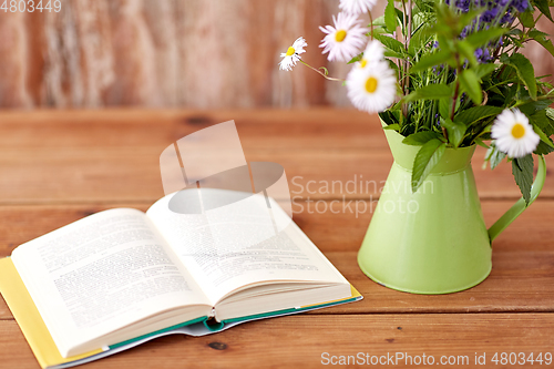 Image of book and flowers in jug on wooden table