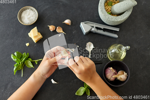 Image of hands peeling garlic with knife for pesto sauce