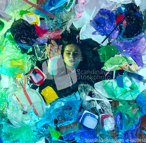 Image of Woman drowning in ocean water under plastic recipients pile, environment concept