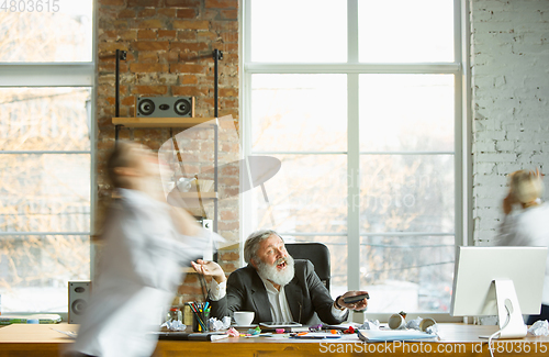 Image of Tired boss resting at his workplace while people moving near blurred