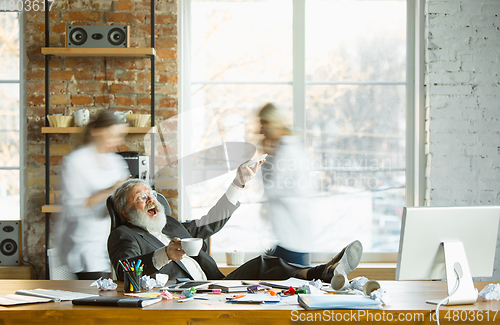 Image of Tired boss resting at his workplace while people moving near blurred