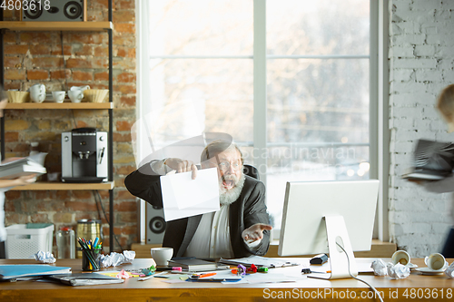 Image of Nervous and tired boss at his workplace busy while people moving near blurred