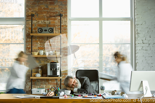 Image of Tired boss resting at his workplace while people moving near blurred