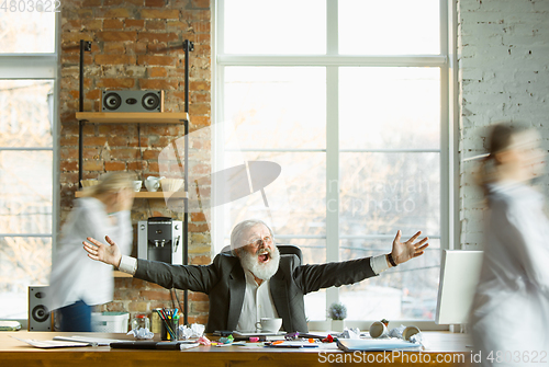 Image of Tired boss resting at his workplace while people moving near blurred