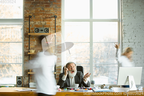 Image of Tired boss resting at his workplace while people moving near blurred