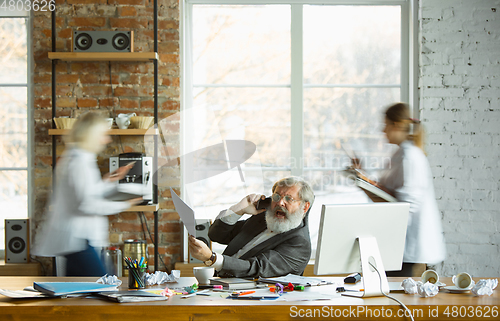 Image of Nervous and tired boss at his workplace busy while people moving near blurred