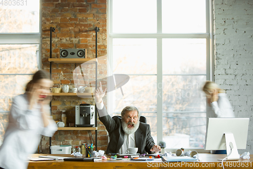 Image of Tired boss resting at his workplace while people moving near blurred