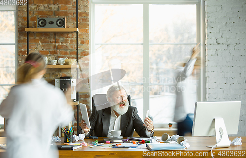 Image of Tired boss resting at his workplace while people moving near blurred