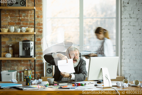 Image of Nervous and tired boss at his workplace busy while people moving near blurred