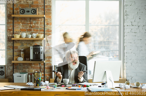 Image of Nervous and tired boss at his workplace busy while people moving near blurred