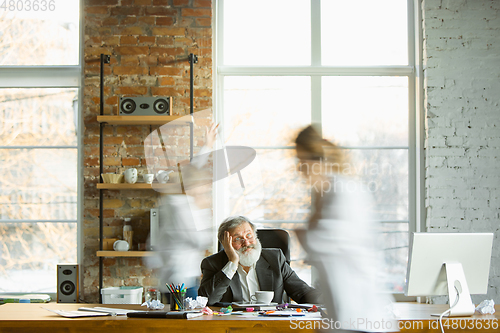 Image of Tired boss resting at his workplace while people moving near blurred