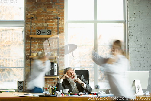 Image of Tired boss resting at his workplace while people moving near blurred