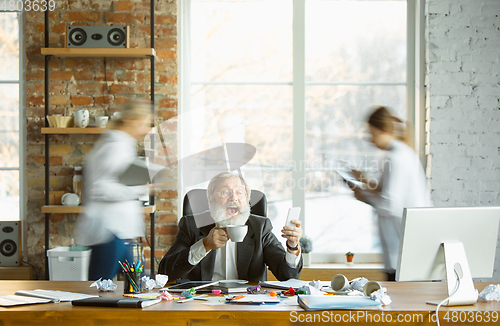 Image of Tired boss resting at his workplace while people moving near blurred