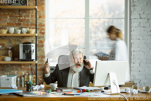 Image of Nervous and tired boss at his workplace busy while people moving near blurred