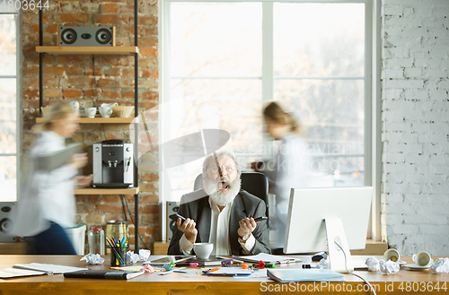 Image of Nervous and tired boss at his workplace busy while people moving near blurred