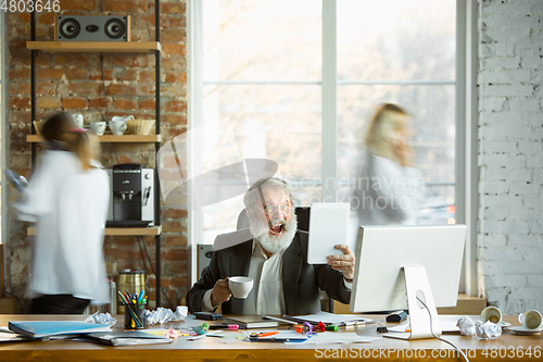 Image of Nervous and tired boss at his workplace busy while people moving near blurred