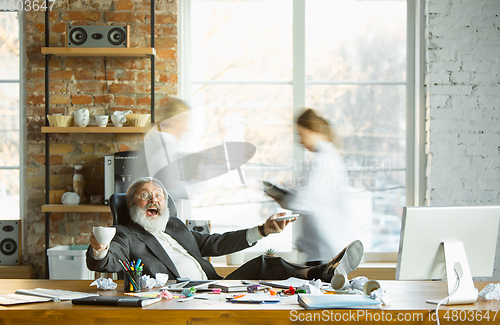 Image of Tired boss resting at his workplace while people moving near blurred