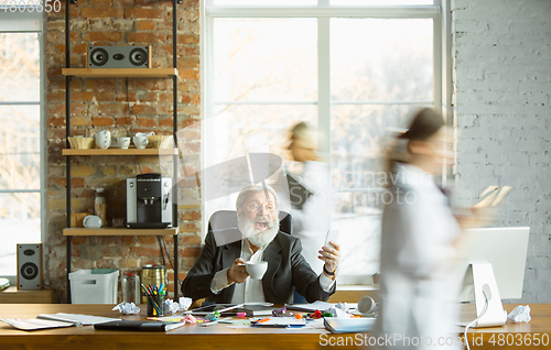 Image of Tired boss resting at his workplace while people moving near blurred