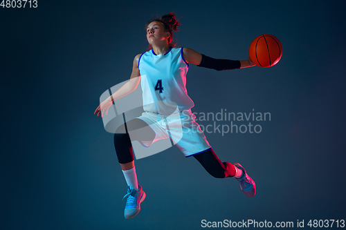 Image of Young caucasian female basketball player on blue studio background in neon light