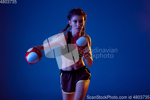 Image of Fit caucasian woman in sportswear boxing on blue studio background in neon light