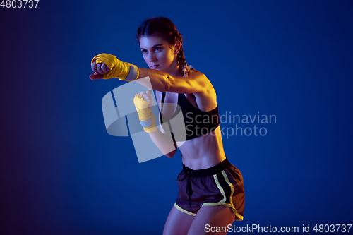 Image of Fit caucasian woman in sportswear boxing on blue studio background in neon light