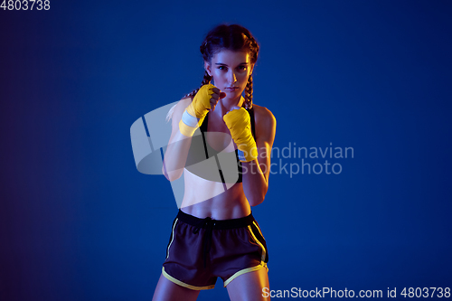 Image of Fit caucasian woman in sportswear boxing on blue studio background in neon light