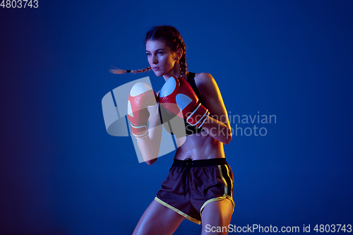 Image of Fit caucasian woman in sportswear boxing on blue studio background in neon light